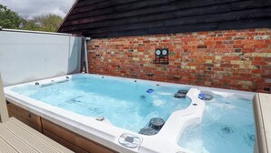 A hot tub with a wooden deck and a brick wall in the background. - Wood Farm Cottage (Boston)