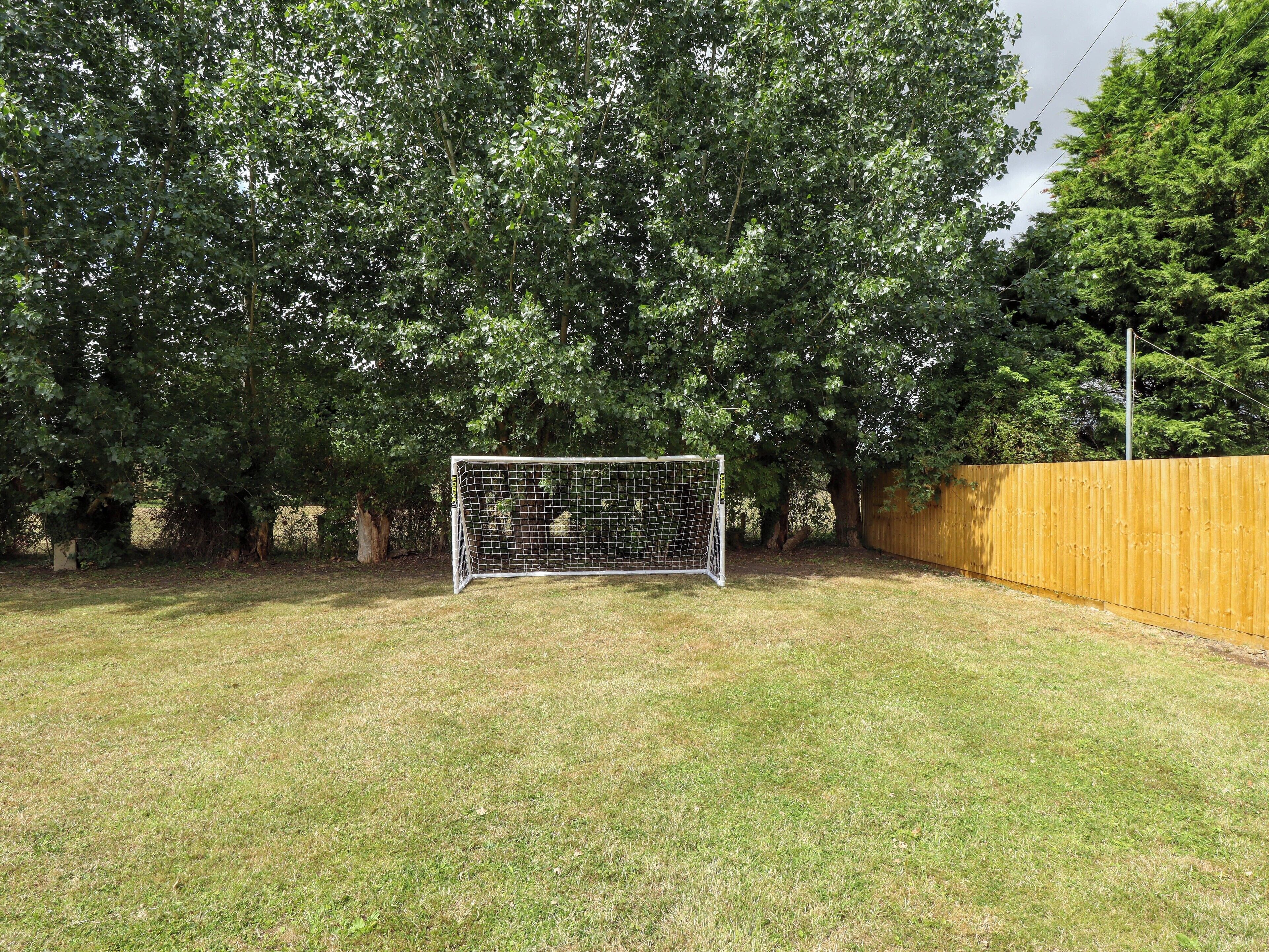 Une cour arrière clôturée avec un but de football, entourée d’arbres et d’une clôture en bois.