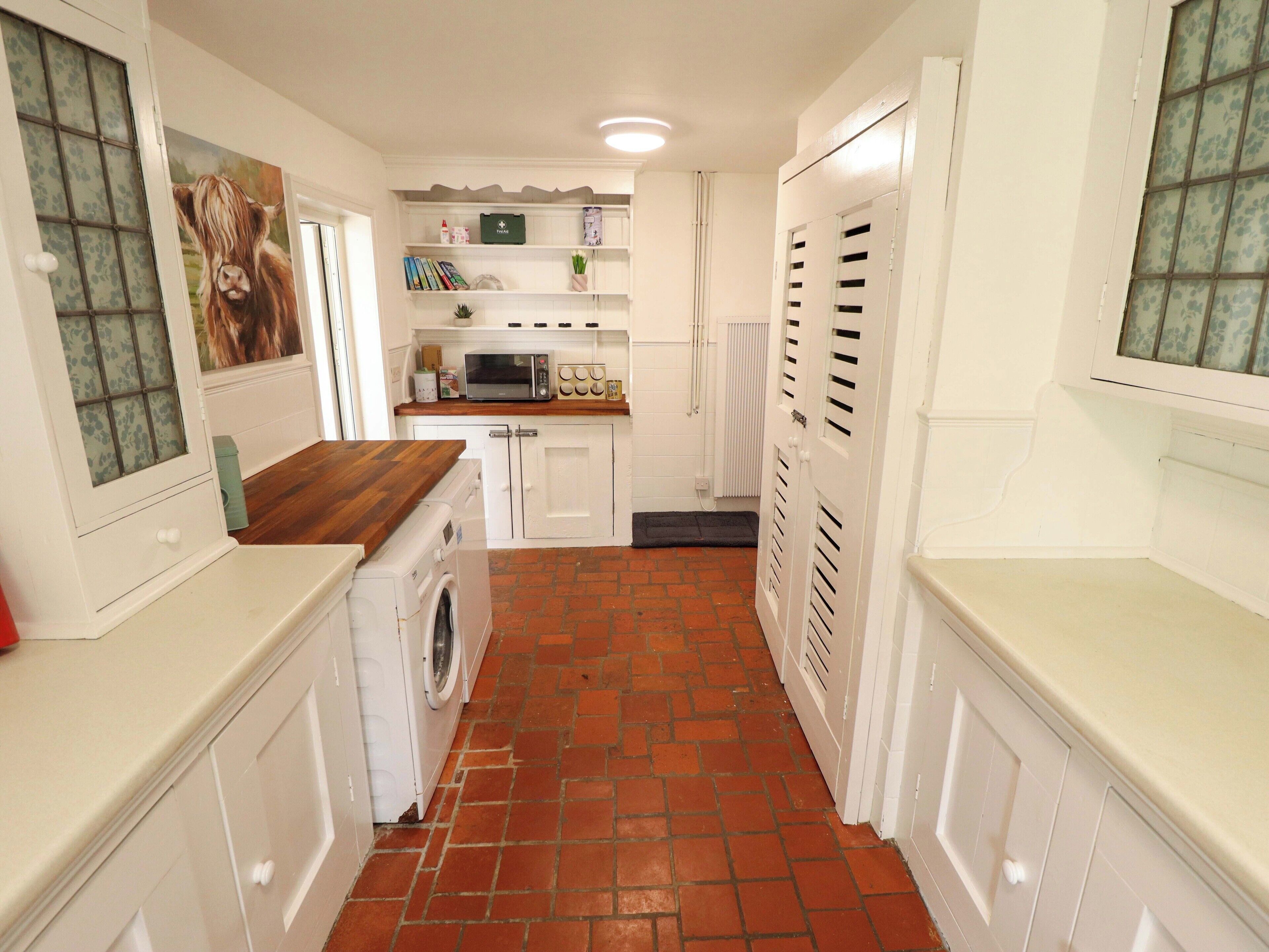 A compact kitchen with white cabinetry, a microwave, a washing machine, and a wooden countertop.