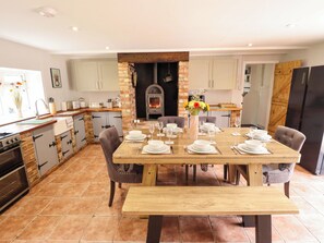 A modern kitchen with a central island, a dining table set for six, and a wood-burning stove. - Wood Farm Cottage (Boston)