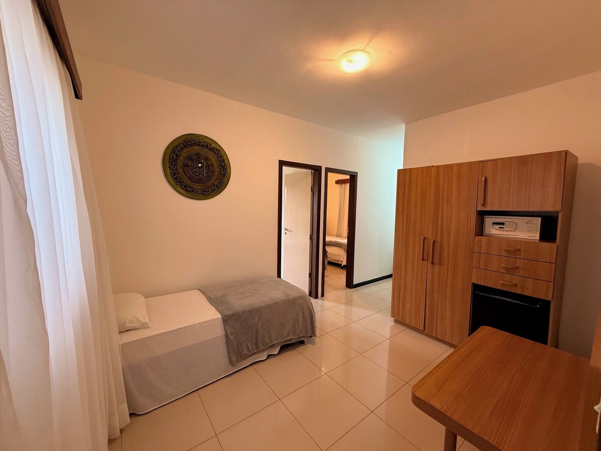 A room with a bed, a wooden wardrobe, a desk, and a mirror.
