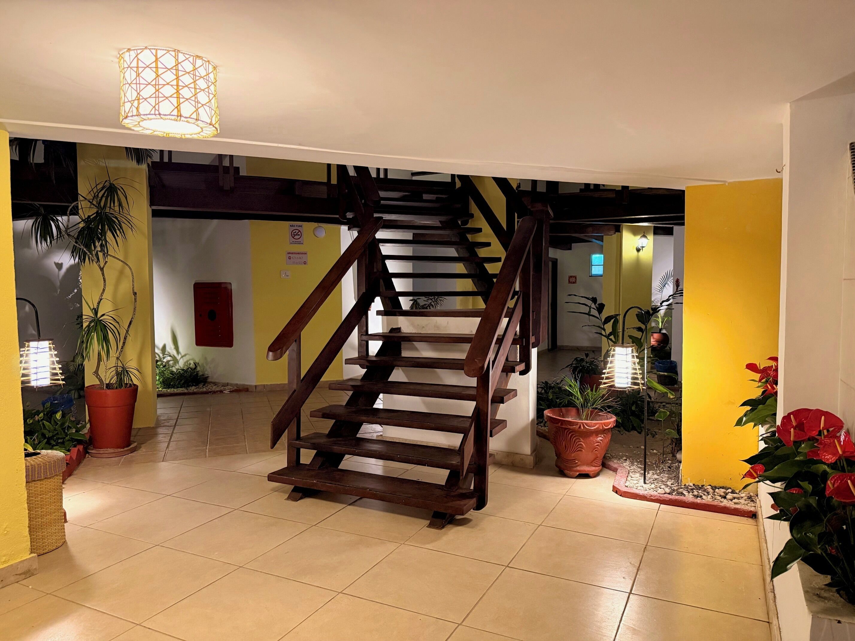 A staircase with wooden railings leading to an upper floor, surrounded by potted plants and a tiled floor.
