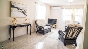 Un salon avec un sol en marbre, un canapé noir, un fauteuil noir, un téléviseur et un tableau accroché au mur.