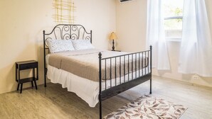 Une chambre à coucher comprenant un lit, une table de chevet, une lampe, un climatiseur et une fenêtre avec des rideaux.