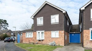 A two-story residential building with a dark brown exterior, white window frames, and a blue garage door. - The Willow - Home with modern facilities in the outstandingly beautiful Surrey (Woking)