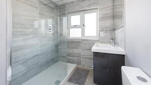 A modern bathroom with a glass shower enclosure, a white sink, and a dark vanity. - The Willow - Home with modern facilities in the outstandingly beautiful Surrey (Woking)