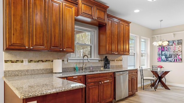 Una cocina con armarios de madera, encimeras de granito, lavavajillas y una zona de comedor con mesa y sillas.