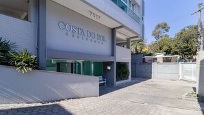 A modern building with the sign 'Costa do Sol Residence'. It features a covered entrance, a bench, and a paved walkway. - 2 Bedroom Apartment With Barbecue Cts0203 (Florianópolis)