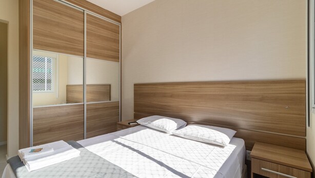 A bedroom with a bed, a nightstand, a wooden wardrobe, and a mirror. - 2 Bedroom Apartment With Barbecue Cts0203 (Florianópolis)