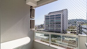 A balcony with a chain-link fence, a white wall, and a view of a modern building in the background. - 2 Bedroom Apartment With Barbecue Cts0203 (Florianópolis)