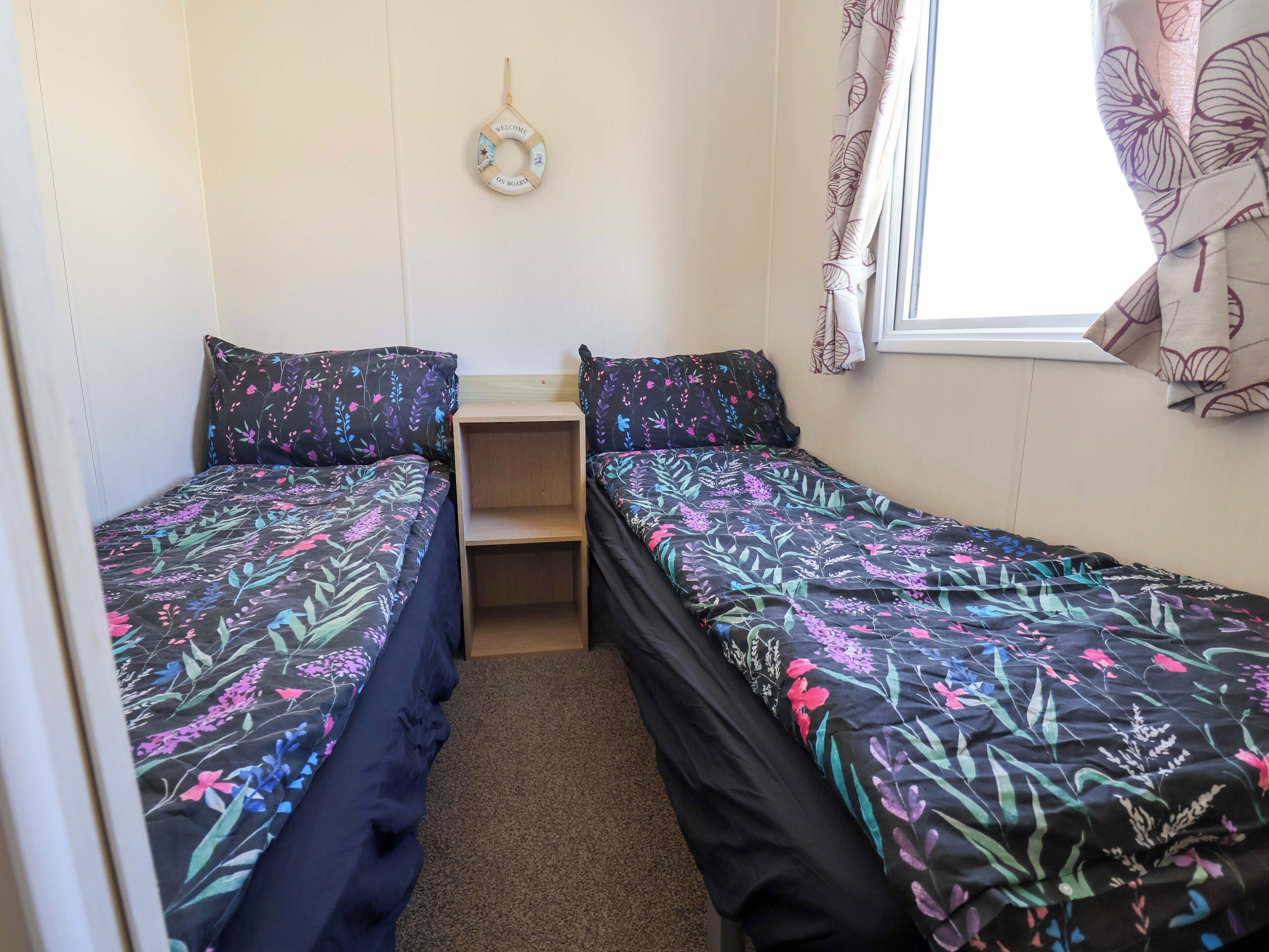 Una habitación pequeña y compacta con dos camas individuales, un estante de madera y un letrero de bienvenida en la pared.