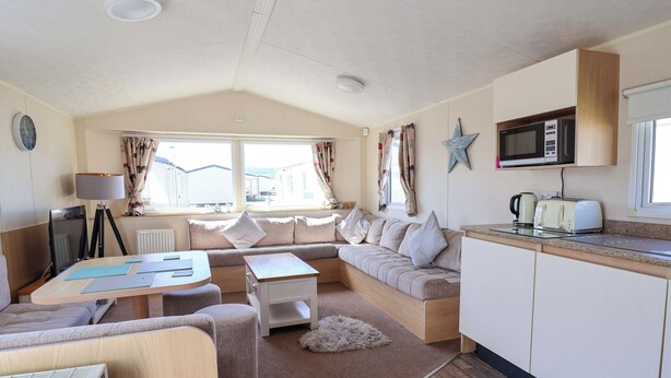 A cozy living area with a sofa, a small table, a kitchen with a microwave, and a view of the outside. - Willerby Aurora B14 (Abergele)