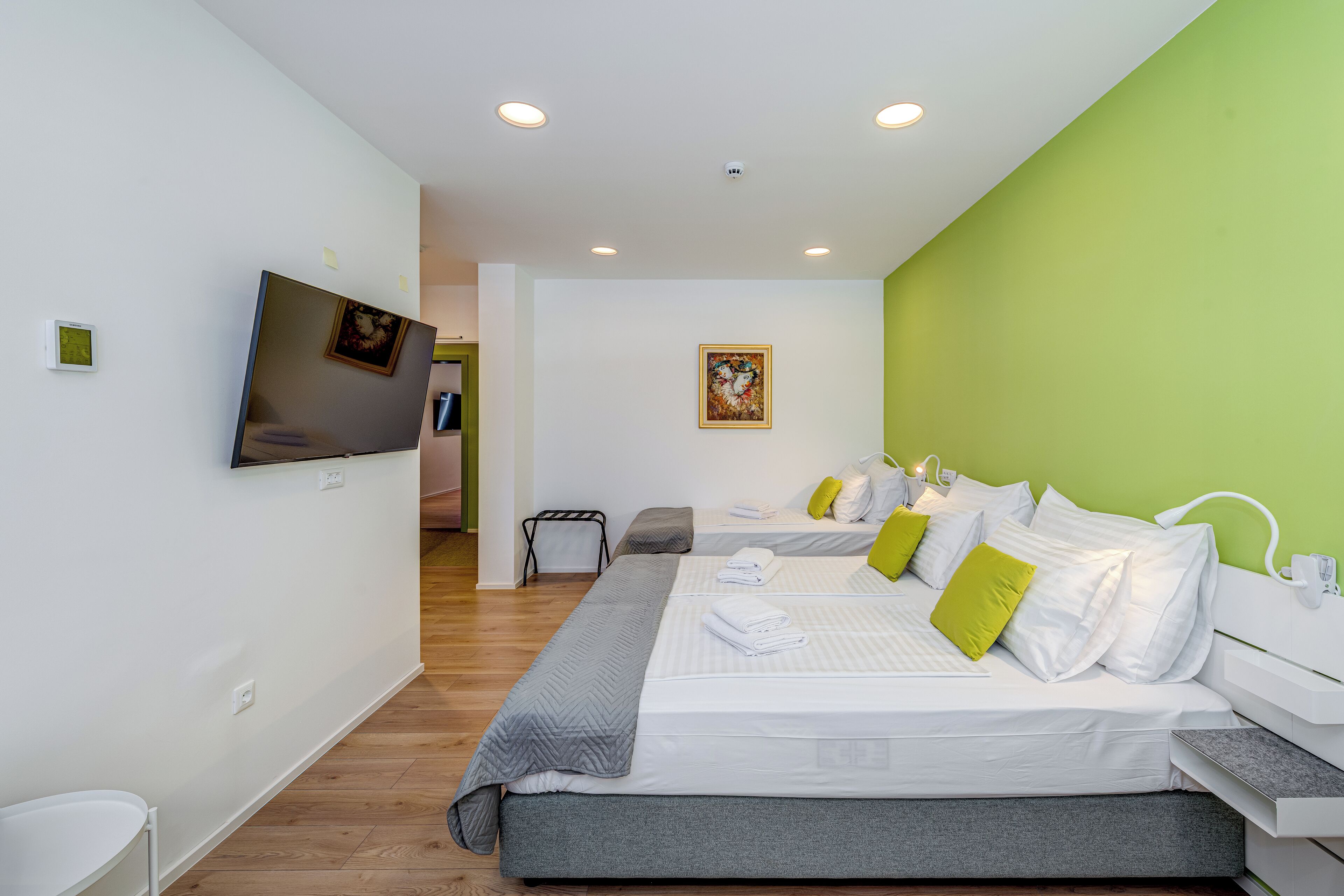 A modern hotel room with a large bed, a television, and a green accent wall.