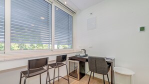 Une cuisine moderne dotée d’un four encastré, d’un petit coin repas avec trois chaises et d’une fenêtre avec des stores.