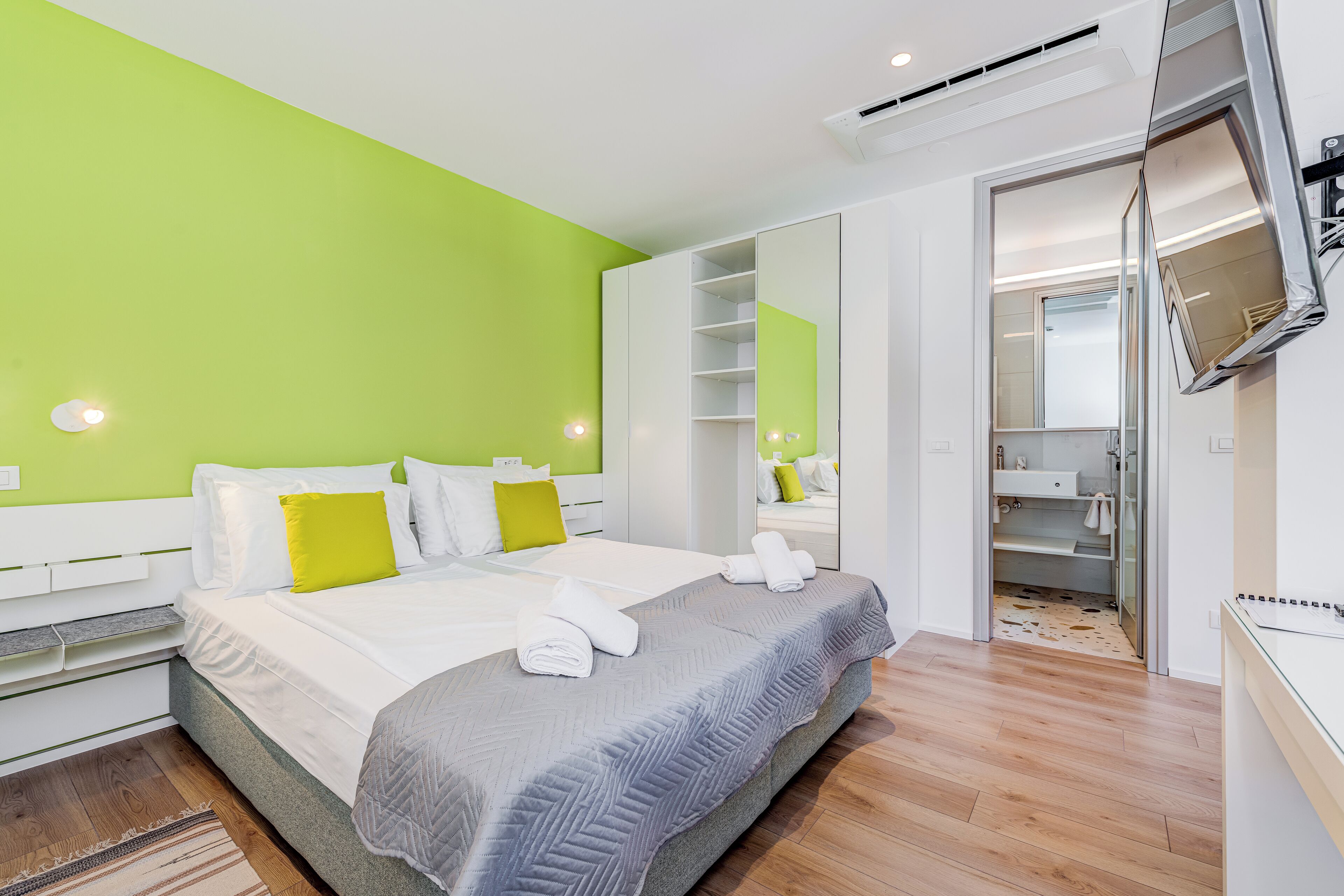 A modern hotel room with a large bed, a walk-in closet, and a bathroom with a mirror and sink.
