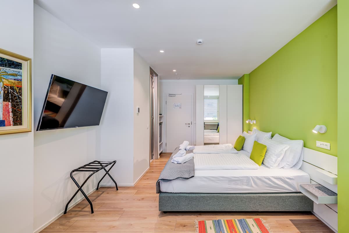 Un dormitorio moderno con dos camas, un televisor montado en la pared y una pared de acento verde.