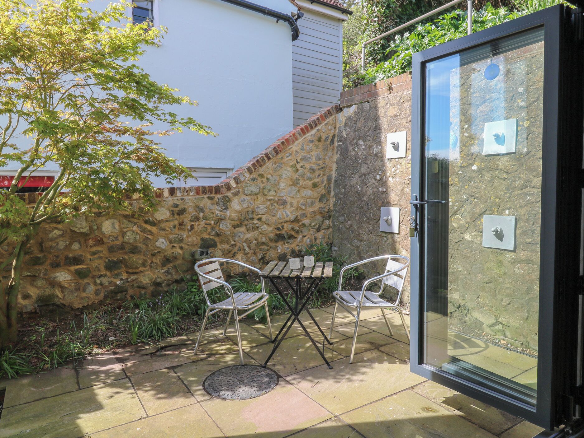 A patio with a stone wall, a glass door, and two metal chairs.