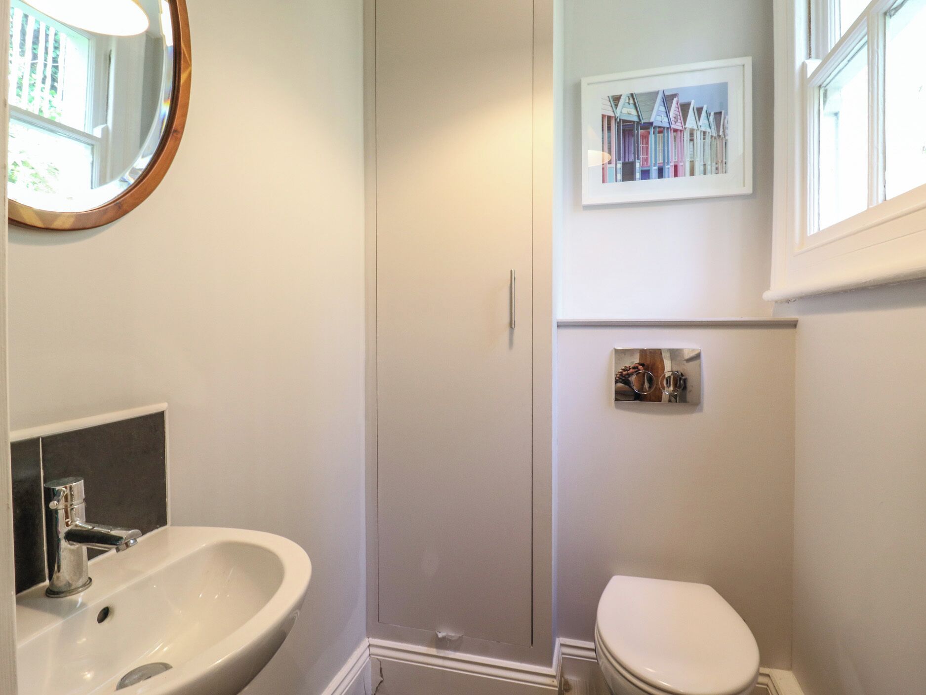 A bathroom with a white sink, a toilet, and a mirror. There is a framed picture on the wall above the toilet.