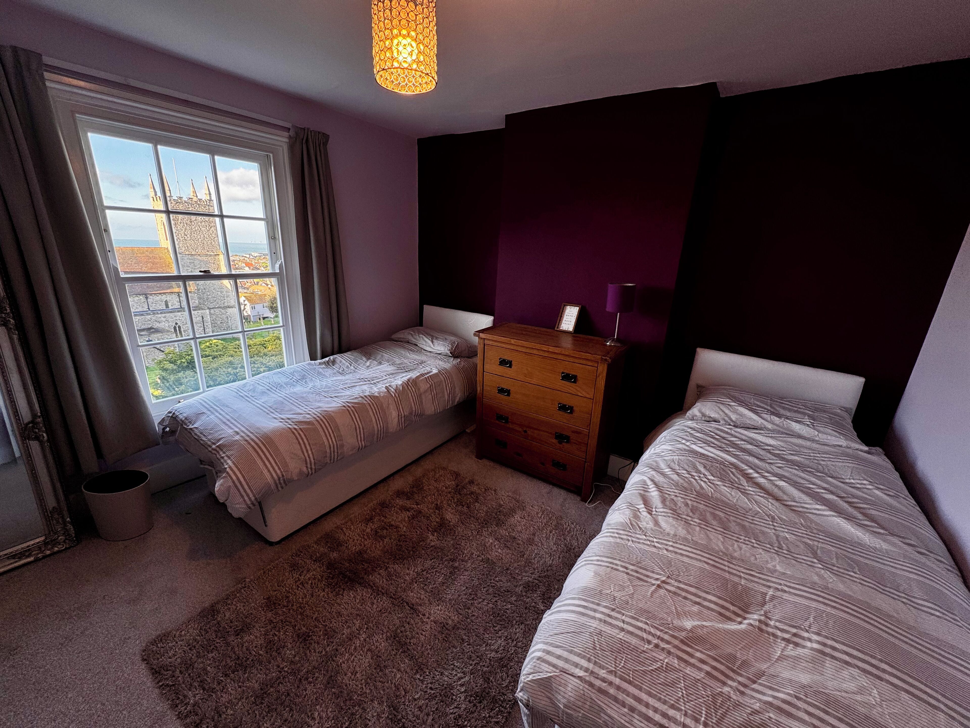 Une chambre avec deux lits, une commode, une fenêtre avec des rideaux et un luminaire suspendu.