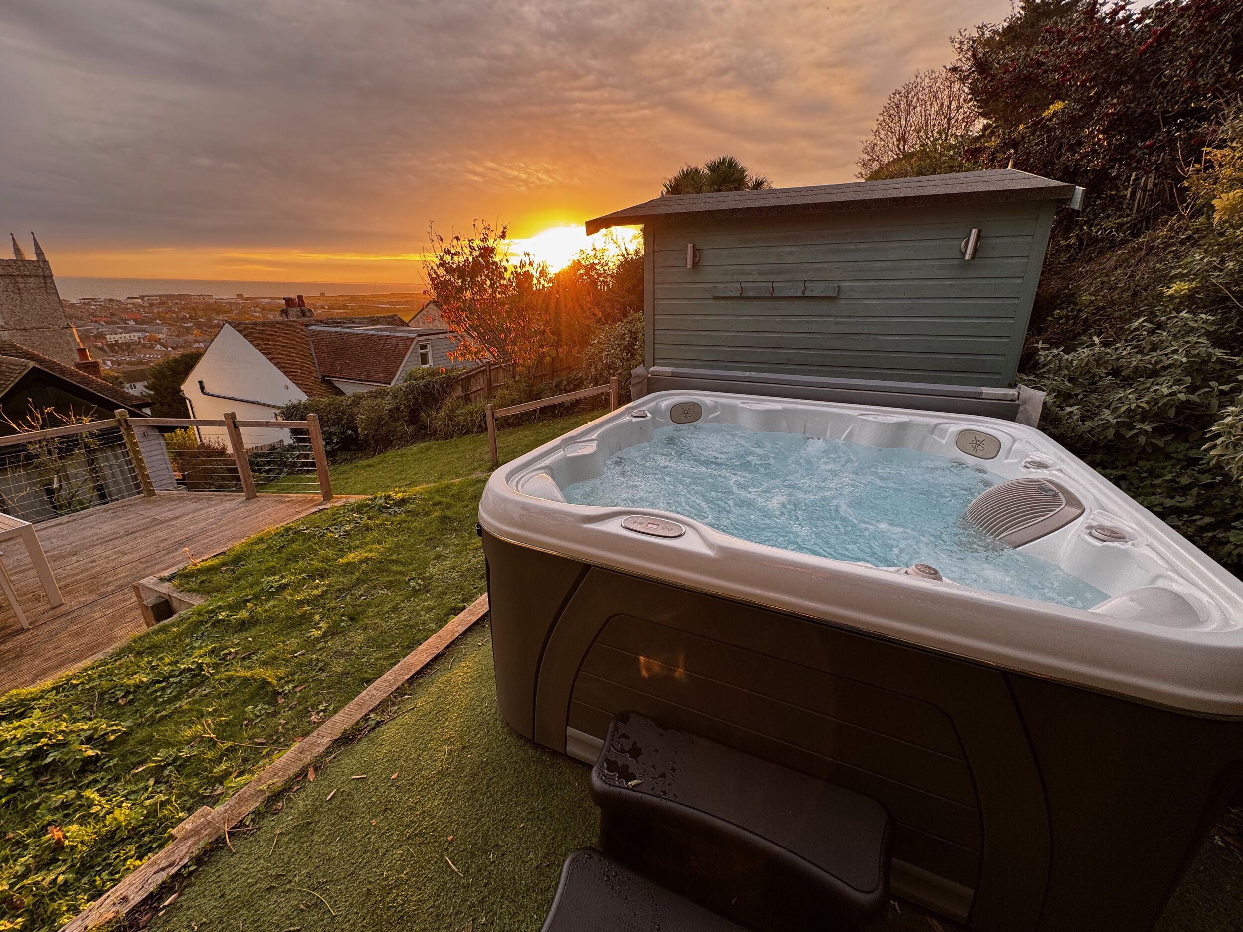 A hot tub with a wooden deck and a view of the sunset.