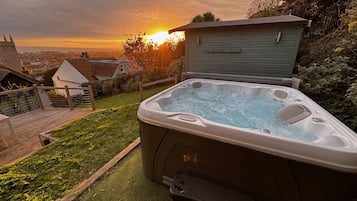 A hot tub with a wooden deck and a view of the sunset.