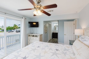 A bedroom with a bed, a ceiling fan, a TV, a dresser, a bathroom, and a balcony. - Private waterfront escape! Open water views & kayaks. Come sail away (Marathon)