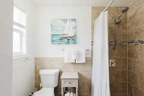 Un baño con inodoro, lavamanos, ducha y un cuadro de un velero.