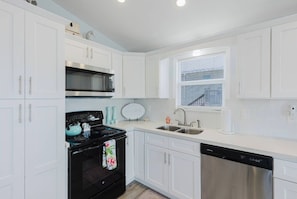 A modern kitchen with white cabinetry, a black stove, a dishwasher, and a window with blinds. - Private waterfront escape! Open water views & kayaks. Come sail away (Marathon)