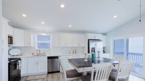 A modern kitchen with white cabinets, a stainless steel dishwasher, and a dining area with a wooden table and white chairs.