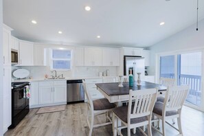 A modern kitchen with white cabinets, a stainless steel dishwasher, and a dining area with a wooden table and white chairs. - Private waterfront escape! Open water views & kayaks. Come sail away (Marathon)