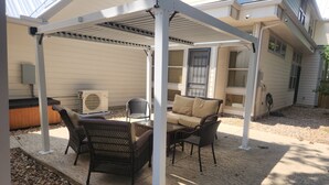En overdækket terrasse med fletningsmøbler, varmelegeme og et vindue med udsigt til huset.