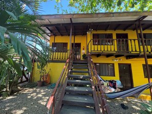 A two-story yellow building with a wooden staircase leading to a balcony. - Hotel Brasilito (Cabo Velas)