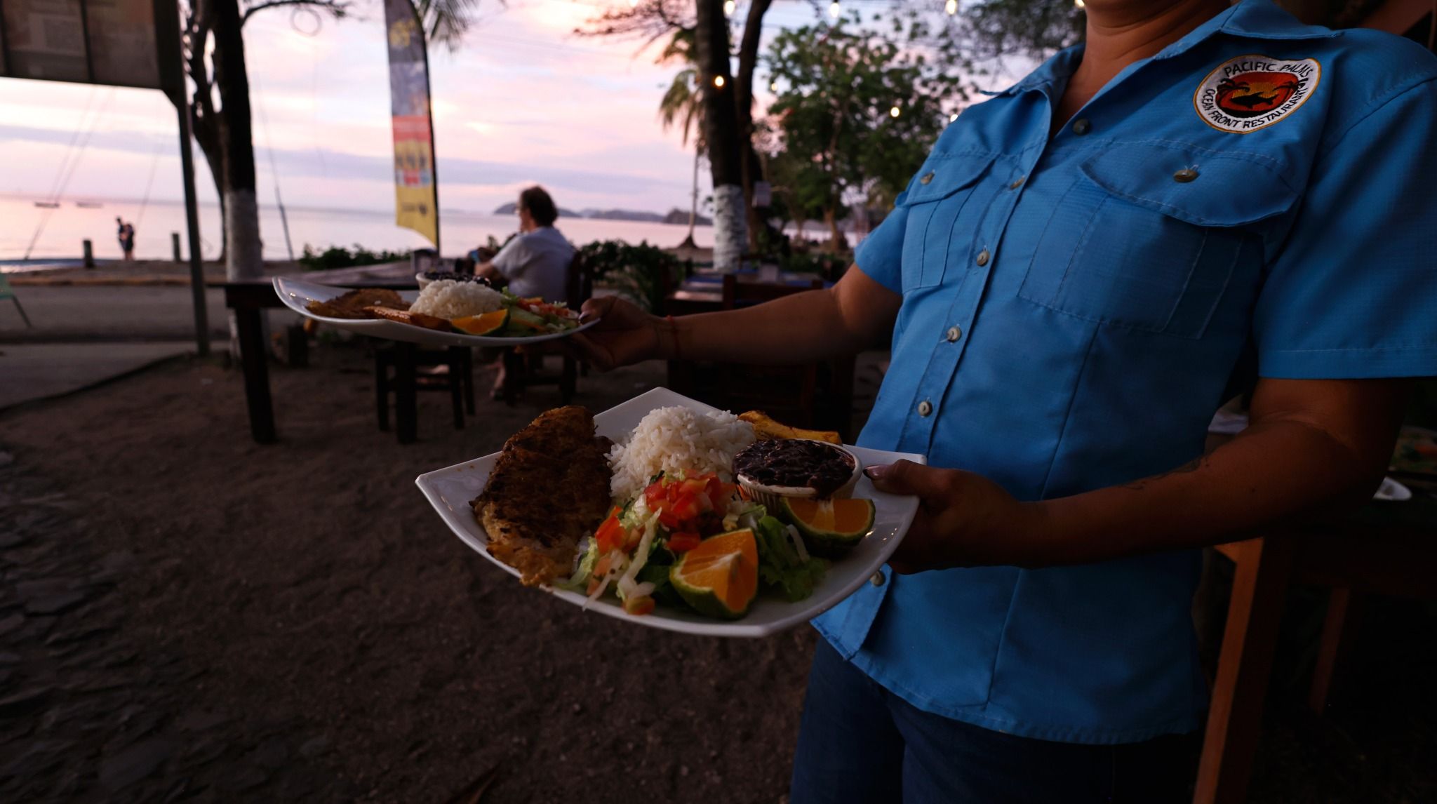 Una persona che tiene un vassoio con cibo, tra cui riso, fagioli e verdure, in un ristorante sulla spiaggia.