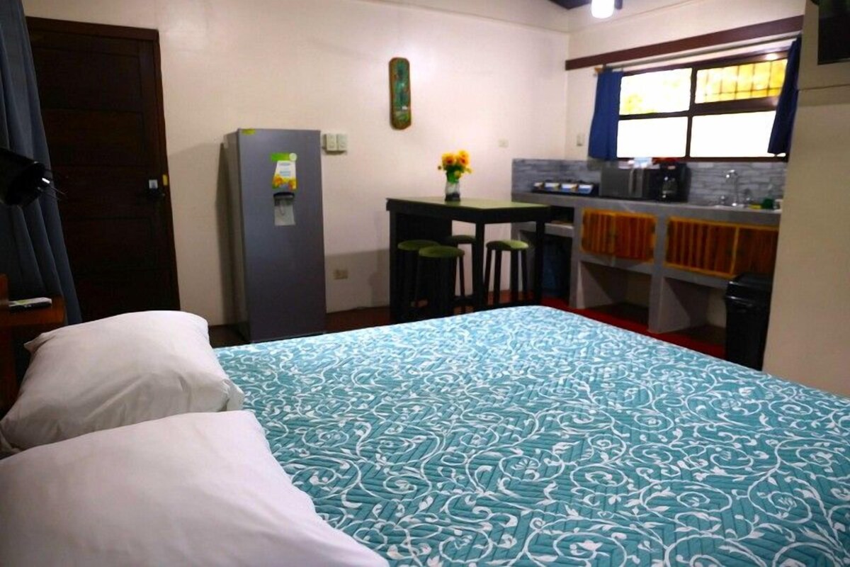A compact hotel room with a bed, a small kitchenette, and a dining area.