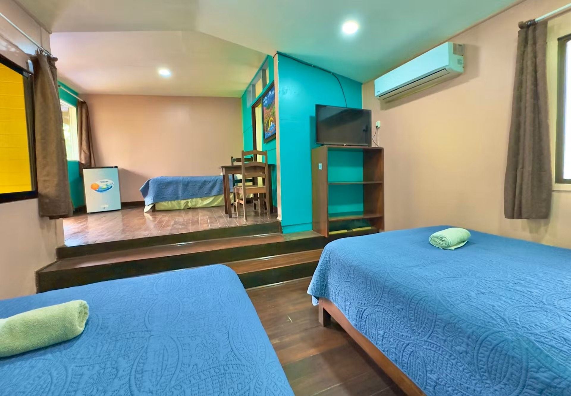A hotel room with two beds, a desk, a chair, a TV, and a staircase leading to another room.