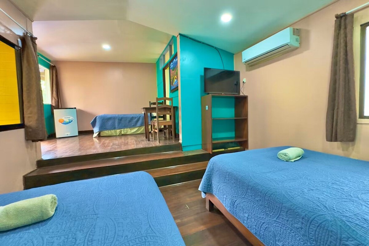 A hotel room with two beds, a desk, a chair, a TV, and a staircase leading to another room.