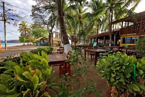 A beachfront restaurant with outdoor seating, palm trees, and a view of the ocean. - Hotel Brasilito (Cabo Velas)