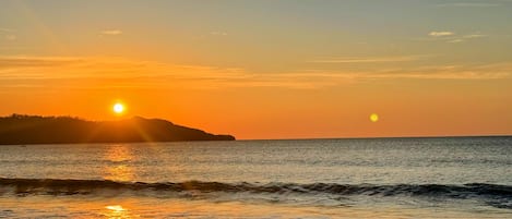 Una playa al atardecer, con el sol reflejándose en el agua.