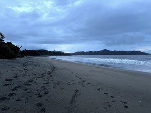 A beach with footprints leading to the water, a distant mountain, and overcast sky. - Hotel Brasilito (Cabo Velas)