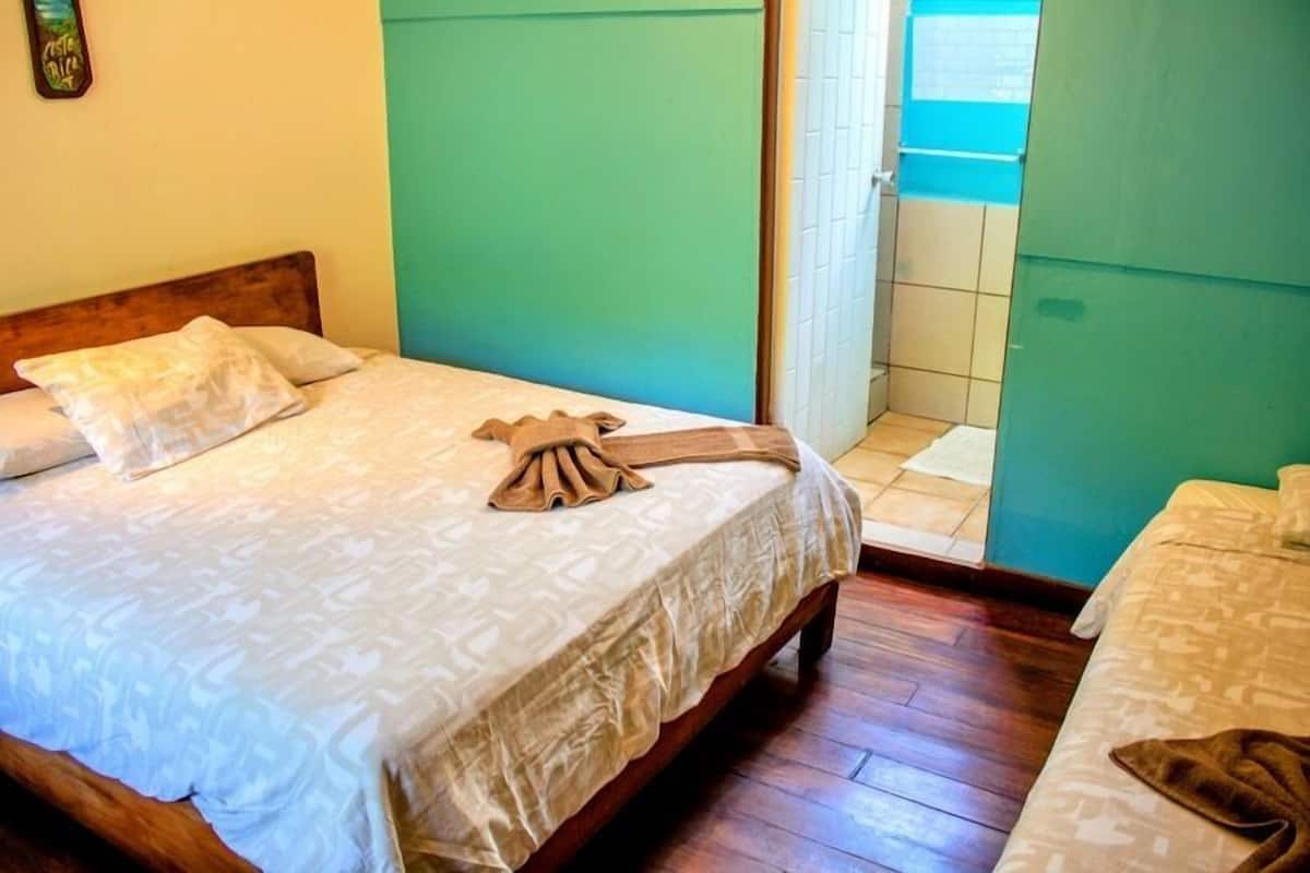 Una habitación con cama, cabecera de madera, manta marrón y una mesita.