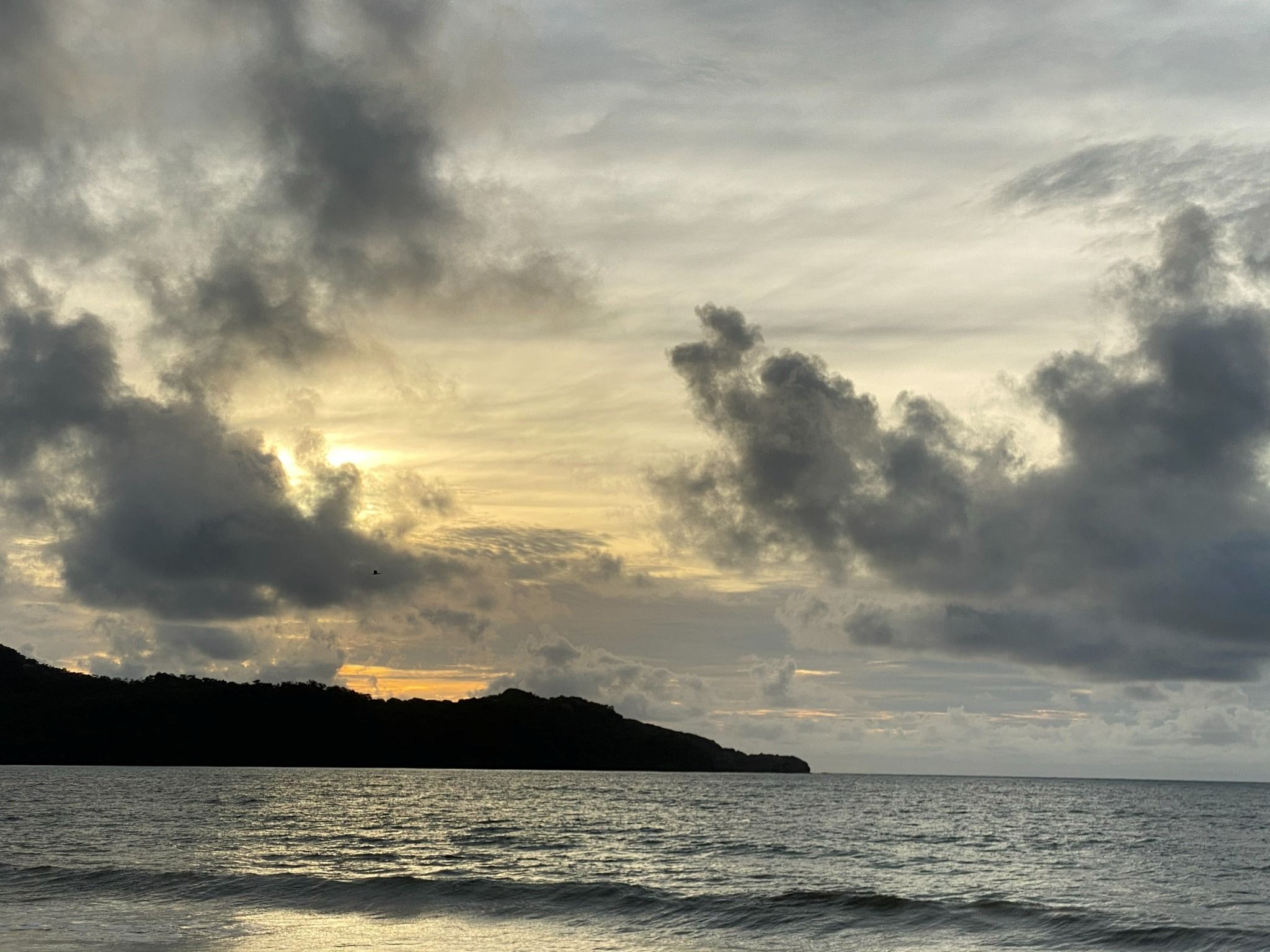 A coastal landscape with a body of water, a hilly terrain, and a cloudy sky.