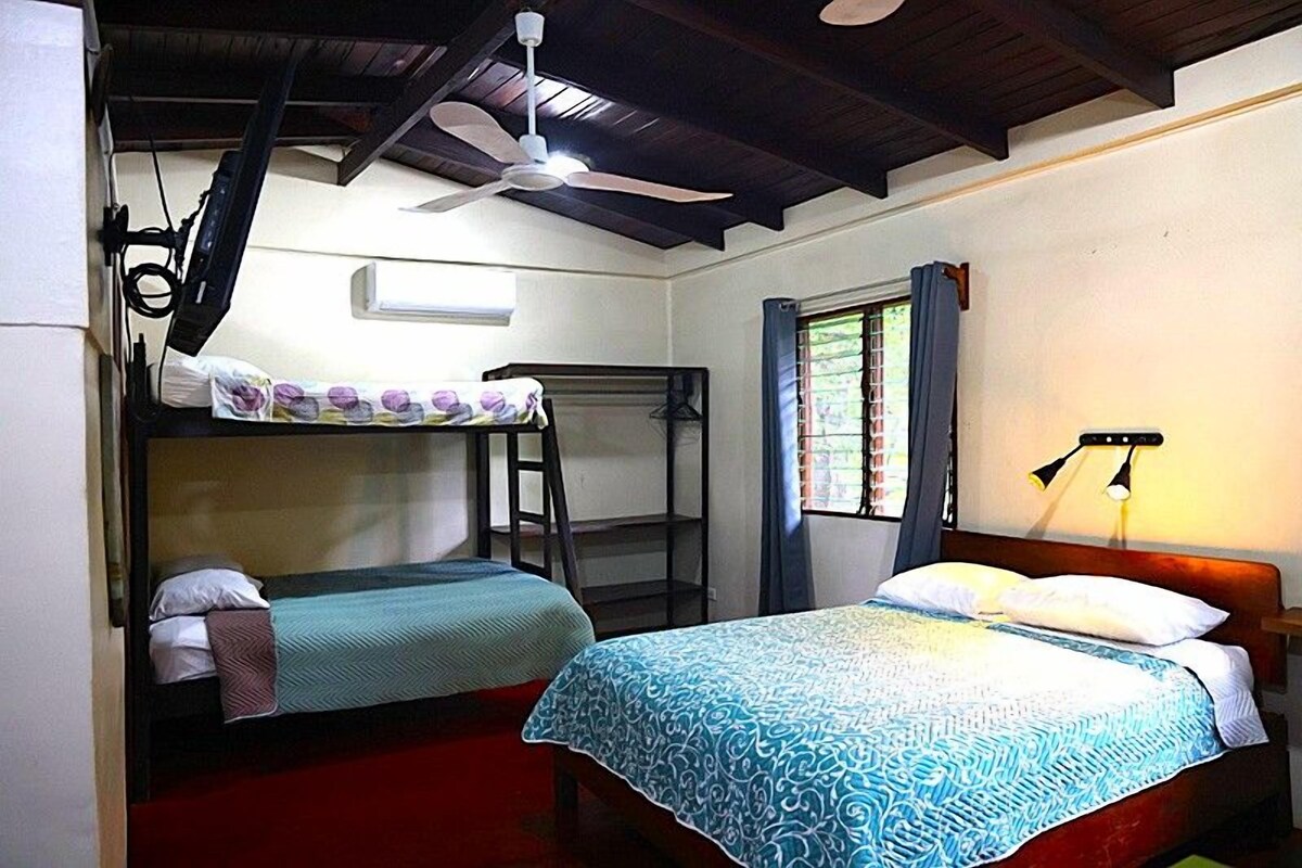 A room with two beds, a ceiling fan, a window with curtains, and a wall-mounted lamp.
