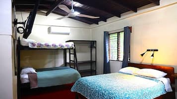 A room with two beds, a ceiling fan, a window with curtains, and a wall-mounted lamp.
