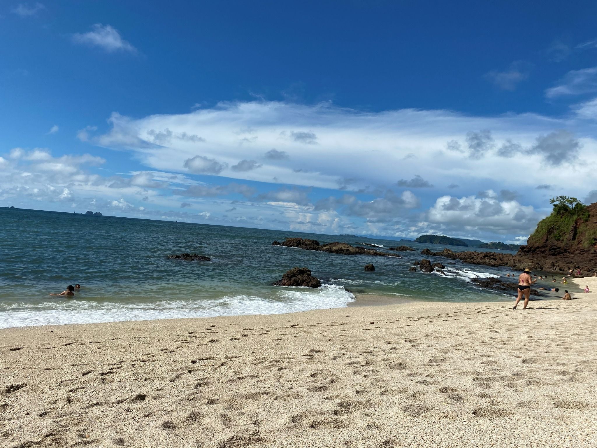 A beach with clear skies, calm water, and rocky outcrops.