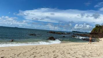 A beach with clear skies, calm water, and rocky outcrops.