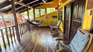 A covered outdoor seating area with wooden flooring, rocking chairs, and a hammock.