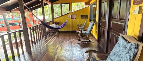 A covered outdoor seating area with wooden flooring, rocking chairs, and a hammock.