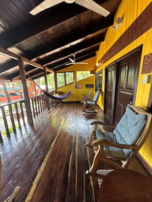 A covered outdoor seating area with wooden flooring, rocking chairs, and a hammock. - Hotel Brasilito (Cabo Velas)