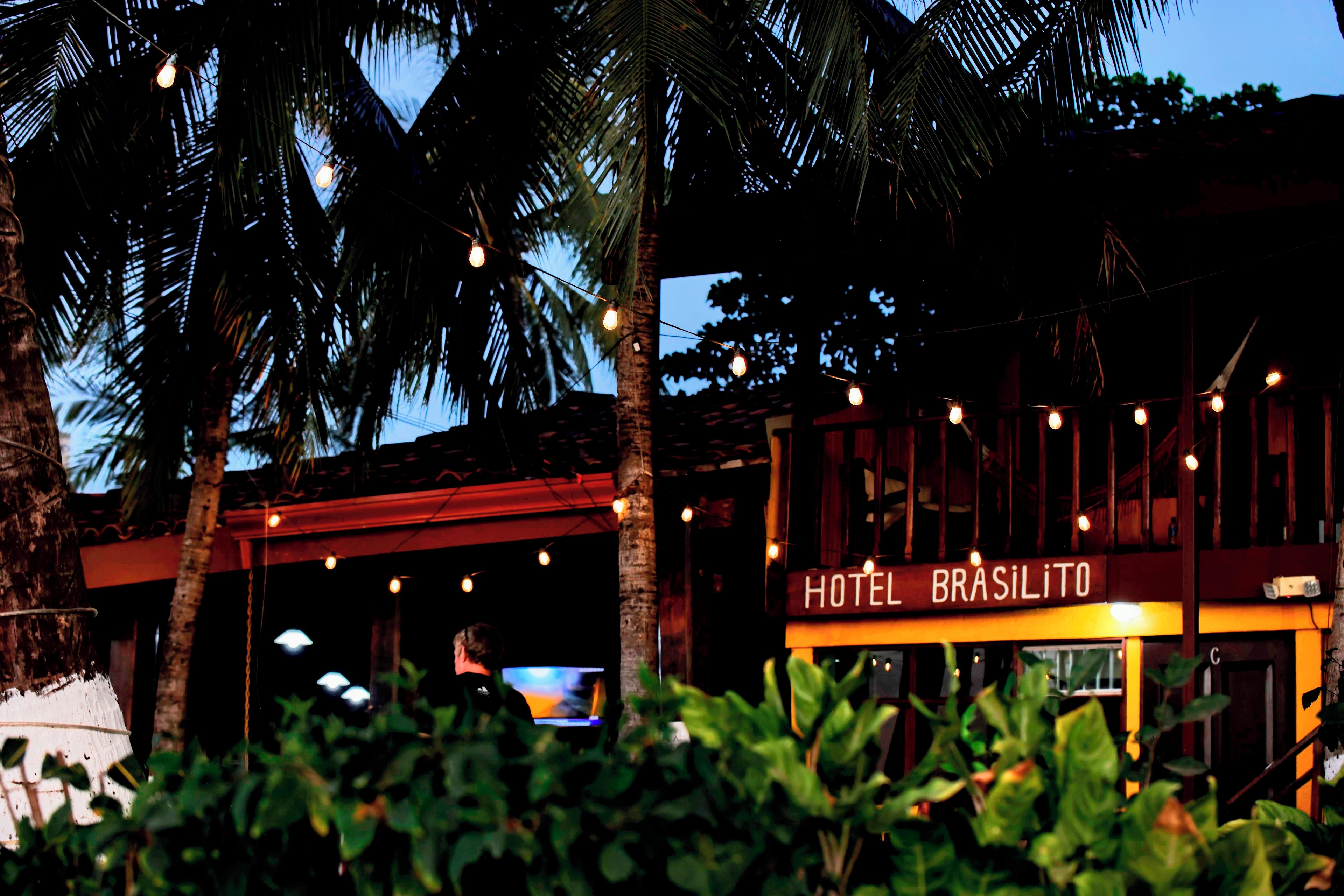 A hotel named "HOTEL BRASILITO" with a red facade, palm trees, and string lights.
