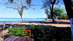 A beachside view with a wooden table and chair, palm trees, and a clear view of the ocean. - Hotel Brasilito (Cabo Velas)